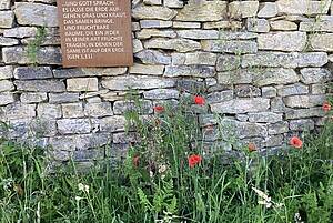 Mauer mit Blumen davor und Infotafel
