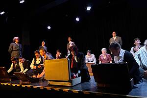 Jugendliche führen ein Theaterstück auf, sie sitzen vor gepackten Koffern auf dem Boden