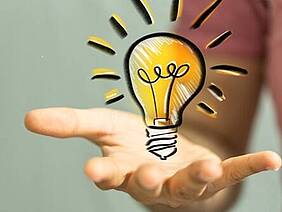 Hand mit einer gezeichneten leuchtenden Glühbirne