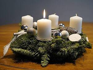Adventskranz mit weißen Kerzen, eine Kerze brennt.